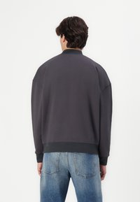 Grå sweatshirt med afslappet pasform, ribbede manchetter og kant. Glat tekstur og rund hals, parret med blå jeans i løs pasform.