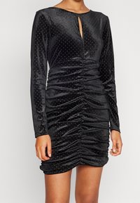 Robe en velours noir à manches longues, avec un décolleté en forme de goutte, un détail froncé et des accents de points argentés dispersés sur toute la surface.