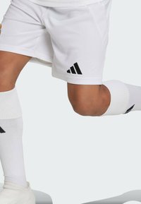 White athletic shorts with black Adidas logo, made of lightweight fabric. Includes white knee-length socks with black accents and ribbed texture.