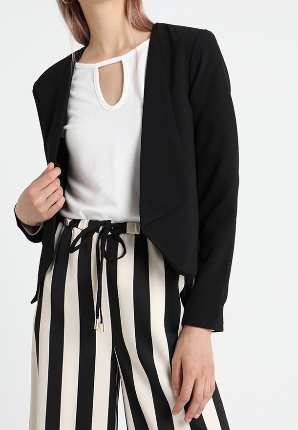 Mustat crop-blazer, jossa on avoin etuosa, yhdistetty valkoiseen toppiin, jossa on avaus kauluksessa, sekä mustavalkoisiin raidallisiin leveälahkeisiin housuihin.