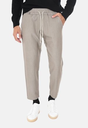 Pantaloni beige con cordino, indossati con calzini neri e sneakers bianche, abbinati a un top nero a maniche lunghe, mostrati dalla vita ai piedi.