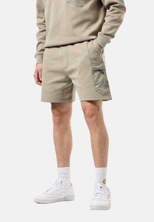 Beige cotton blend shorts with a side cargo pocket and logo detail. Paired with white sneakers and textured ankle socks.