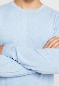 Light blue long-sleeve T-shirt made of soft fabric, featuring a crew neck and ribbed cuffs. Subtle logo on the chest. Smooth texture.