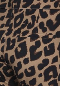 Béžová látka s černým a hnědým leopardím potiskem. Obsahuje skrytou zadní kapsu se rovnými stehy. Měkká textura.