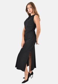 Vestito nero senza maniche con corpetto aderente, una gonna lunga e fluida, e uno spacco laterale fino alla coscia, abbinato a tacchi a punta neri.