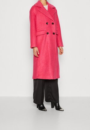 Roze dubbelzijdige jas met grote zwarte knopen, met een gelote kraag, zijzakken en een zachte structuur, gecombineerd met zwarte wijde broek.