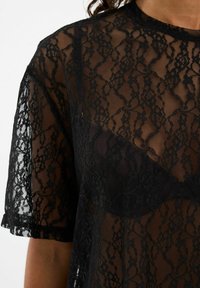 Melnas mežģīņu blūze ar caurspīdīgu dizainu, īsām piedurknēm, ziedu rakstu un noapaļotu apkakli, daļēji atklājot apakšveļu.