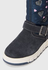 Mørkeblå ruskindsankelstøvle med en tekstureret gummisål. Overdelen har en blå nylon skaft med hjerte- og stjernemønstre. Metalspænde accent.
