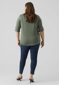 Olijfgroen top met driekwartmouwen, gecombineerd met donkerblauwe skinny jeans. De top heeft een gebogen zoom en een zachte stofstructuur.