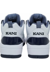 Bílé a námořnické sportovní boty s hladkým koženým svrškem, texturovanou síťovinou a lesklým námořnickým akcentem na patě. Značka je umístěna na zadní straně.