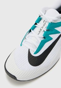 Weißer Sportschuh mit schwarzem Swoosh-Logo, strukturiertem Stoff, türkisfarbenen Akzenten und Zickzack-Design an der Außenseite, ausgestattet mit flachen Schnürsenkeln.