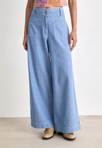 Light blue, wide-leg trousers made of soft denim. Features a button closure, two back pockets, and a relaxed fit with a hemmed edge.