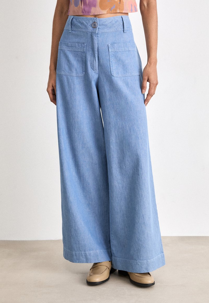Light blue, wide-leg trousers made of soft denim. Features a button closure, two back pockets, and a relaxed fit with a hemmed edge.