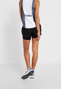 Shorts de sport noirs avec un tissu texturé et un débardeur blanc avec un dos en mesh gris et un logo imprimé sur la partie supérieure.