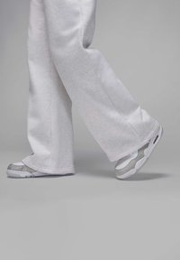 Pantalones de chándal grises combinados con zapatillas que tienen un acento plateado brillante, una base blanca y una forma de punta redondeada. Las zapatillas tienen una textura suave.