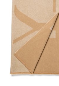 Couverture en laine beige clair avec un motif subtil. Les bords sont à franges. Un coin est replié pour révéler la texture et le design de l'envers.