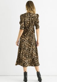 Leopard print dress featuring a cinched waist, puff sleeves, and a mid-length hem, made of soft material. Paired with black chunky-heeled boots.
