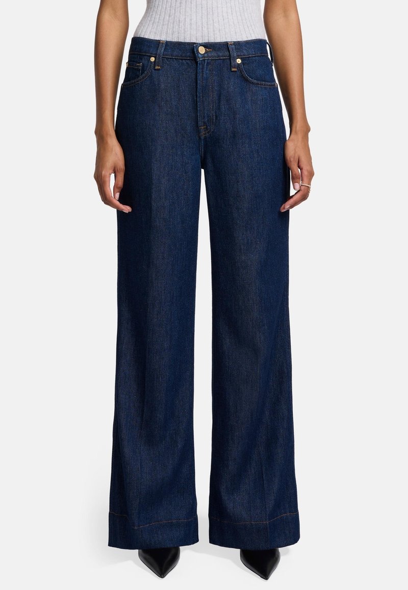 Weite Jeans aus Denim in Dunkelblau. Mit hoher Taille, vorderen Taschen und sichtbaren Nähten. Kombiniert mit spitzen schwarzen Absätzen.