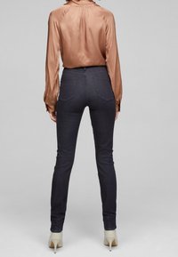 Vaqueros ajustados de mezclilla oscura con una cintura alta, bolsillos traseros y una textura suave, combinados con una blusa de manga larga de color óxido y suave.
