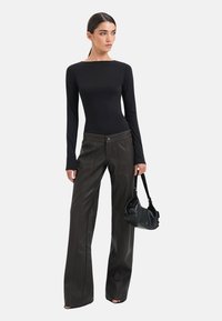 Sort langærmet top parret med mørkebrune viddebukser med lodret syning og en slank sort håndtaske. Glat tekstur over det hele.