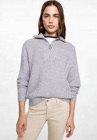 Light gray knitted sweater with a half-zip collar, ribbed texture, and a boxy fit, paired with light beige pants.