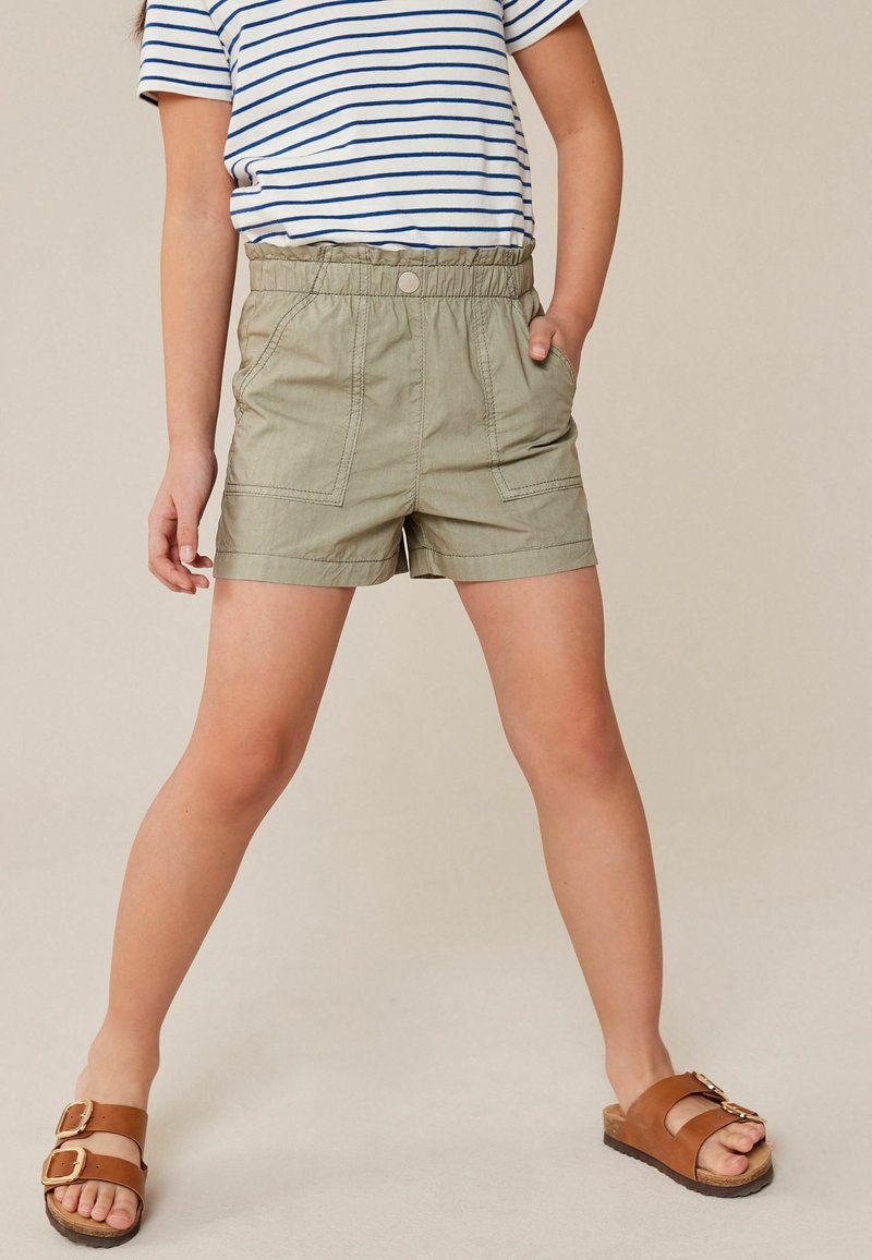 Gröna lätta shorts med framfickor och elastisk midja. Matchas med en randig kortärmad skjorta och bruna slidesandaler.