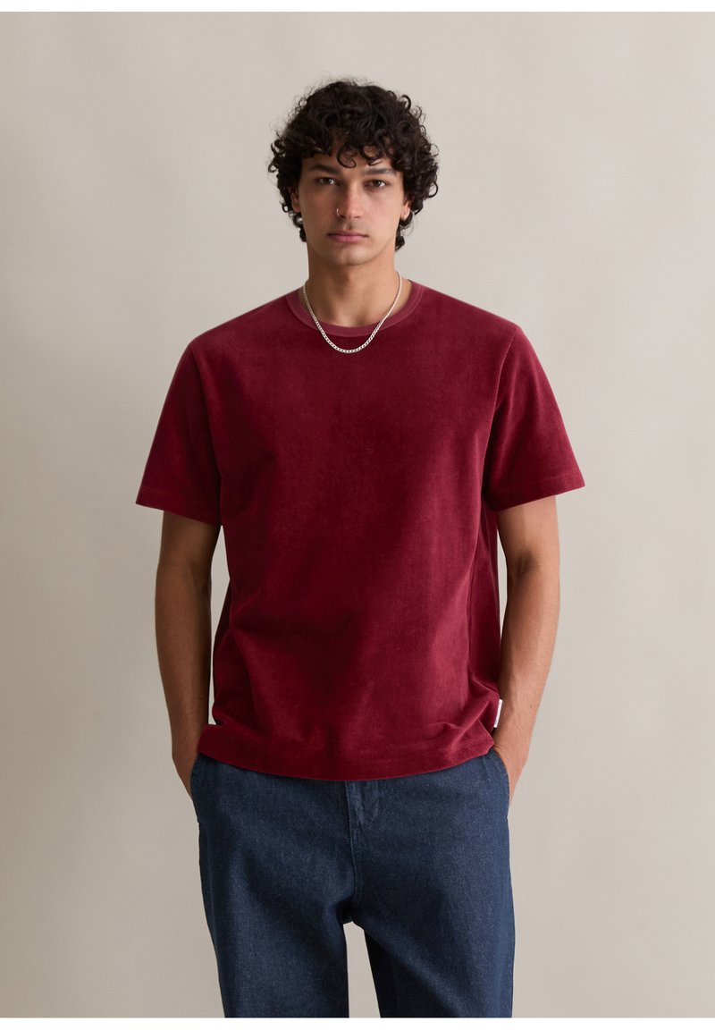 Burgundowa bawełniana koszulka z krótkim rękawem, okrągłym dekoltem i luźnym krojem. Nosić z ciemnoniebieskimi dżinsami.