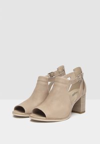 Talons ouverts beiges avec dessus en maille texturée, designs à découpes et un talon bloc avec des rayures horizontales. Bride de cheville ajustable incluse.