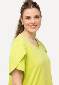 Limegrøn t-shirt med korte ærmer, rund halsudskæring og flæsedetaljer på ærmerne, lavet af blødt, letvægts bomuldsstof.