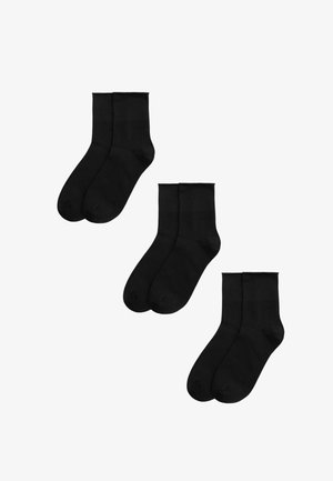 Tres pares de calcetines tobilleros negros lisos dispuestos por separado sobre un fondo blanco.