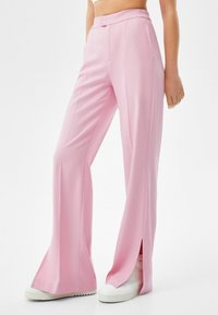 Pink, high-waisted trousers with a loose fit, featuring side slits at the hems and a smooth, lightweight fabric texture.