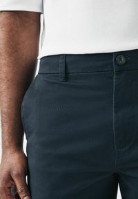 Pantalones de algodón azul marino con una textura suave, que cuentan con un bolsillo frontal, pasadores para cinturón y un cierre de un solo botón.