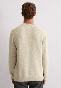 Beiger Strickpullover mit strukturiertem Finish, runder Ausschnitt und gerippten Bündchen. Verfügt über ein dezentes Muster und ein Etikett an der Seite.