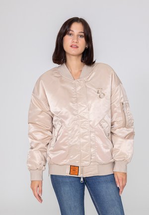 Satinowa bomberka w jasnym beżu, z zapięciem na zamek, bocznymi kieszeniami, ściągaczami przy mankietach oraz pomarańczową metką z przodu.