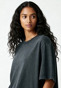 Tricou negru oversized, fabricat dintr-un material moale; are un guler tip crew și mâneci scurte, cu un design subtil de textură spălată.