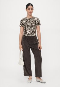 Top a maniche corte a strisce zebrate marroni e crema, pantaloni larghi in corduroy marrone, borsa bianca e scarpe basse di colore chiaro.