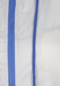 Un tessuto bianco con una superficie liscia presenta una cerniera blu e un cordino blu intrecciato. Le cuciture sono ben definite e tracciano chiaramente i dettagli del design.