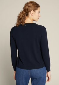 Navy sweater met lange mouwen, geribbelde manchetten en tailleband. Heeft een klein logo-detail op de achterkant van de hals en een gladde textuur.