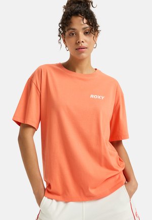 T-shirt Roxy corail à manches courtes en coton doux avec un col rond et un logo blanc sur la poitrine gauche. Coupe décontractée.