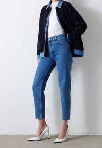 Světle modré džíny s vysokým pasem, doplněné námořnicky modrým sakem s džínovým límcem. Outfit doplňují bílé lodičky na podpatku.