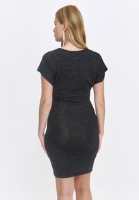 Czarna, krótko rękawowa sukienka o dopasowanym kroju, uszyta z błyszczącego, teksturowanego materiału. Tył ma gładki design i długość do połowy uda.