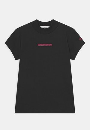 Sort bomuld t-shirt med korte ærmer. Har et rektangulært logo i rød tekst "CALVIN KLEIN JEANS" på forsiden og et lille logo på ærmet.