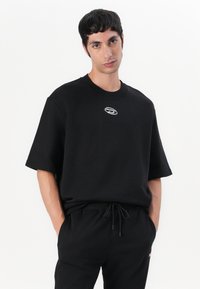 Black short-sleeve t-shirt made of cotton, features a round neck and a small embroidered logo on the chest. Worn with matching sweatpants.