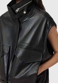 Gilet in pelle nera con colletto alto, chiusura con zip e due grandi tasche frontali. Texture liscia con una finitura lucida.