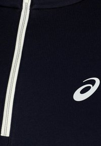 Navy blauwe zip-up jas van gladde stof; heeft een witte rits en een wit logo aan de linkerkant.
