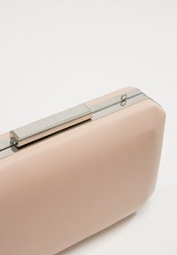 Pochette beige rectangulaire avec surface lisse et fermoir métallique argenté sur le dessus, sur fond uni.