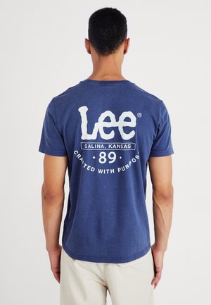 Tumesinise lühikeste varrukate ja puuvillast t-särk, millel on seljal suur valge logo tekstiga "Lee Salina, Kansas 89 Disainitud eesmärgiga."