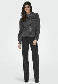 Camisa de mezclilla negra con botones, mangas abullonadas y dos bolsillos frontales, combinada con pantalones rectos a juego y botas de tacón negras.