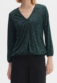 Blusa nera con scollo a V, caratterizzata da motivi astratti verdi. Maniche lunghe con polsini elastici e vita leggermente arricciata per un fit rilassato.