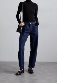 Vysoké džínové kalhoty tmavě modré barvy se uvolněným střihem, zkombinované s přiléhavým černým rolákem a černými mokasíny se zlat ými akcenty.